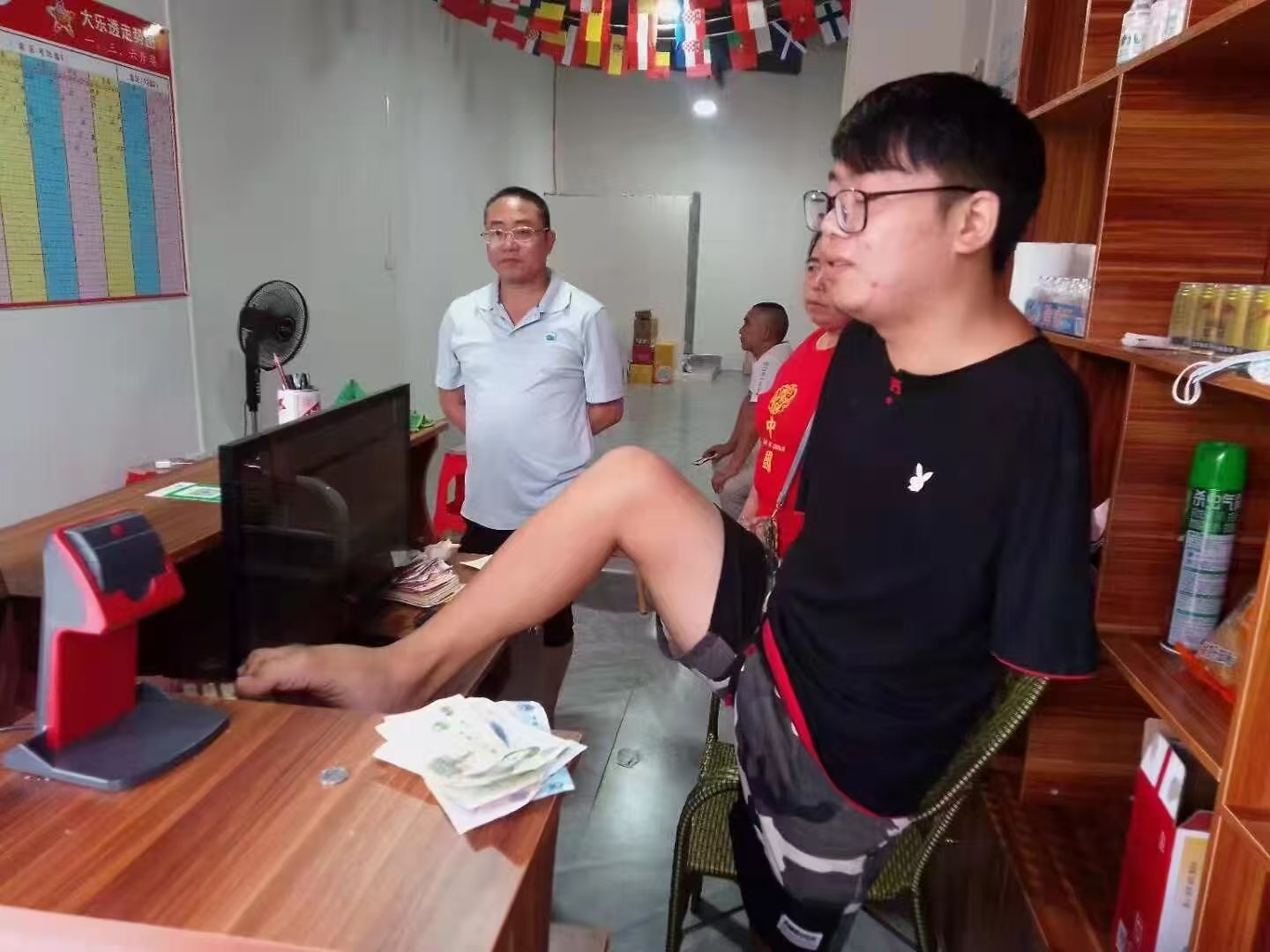 张进（左一）积极协调遵义市相关部门播州区龙坑镇因电击失去双臂的肢残人王小东争取到体彩销售设备，并手把手教会了王小东用双脚机打体育彩票，依靠销售体育彩票走上自食其力的道路。.png