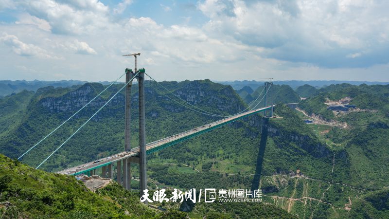 891401-2025年7月6日，位于贵州省安顺市关岭县的在建世界第一高桥—花江峡谷大桥建设正酣，目前已进入桥面铺装阶段，同步推进防撞护栏安装等附属设施施工。花江峡谷大桥兼具交通与旅游价值，其雄伟身姿本身即为景观，每日都有陆陆续续慕名而来观赏大桥的游客，桥旅融合下，游客可通过观景平台、特色步道等，沉浸式感受“天.jpg